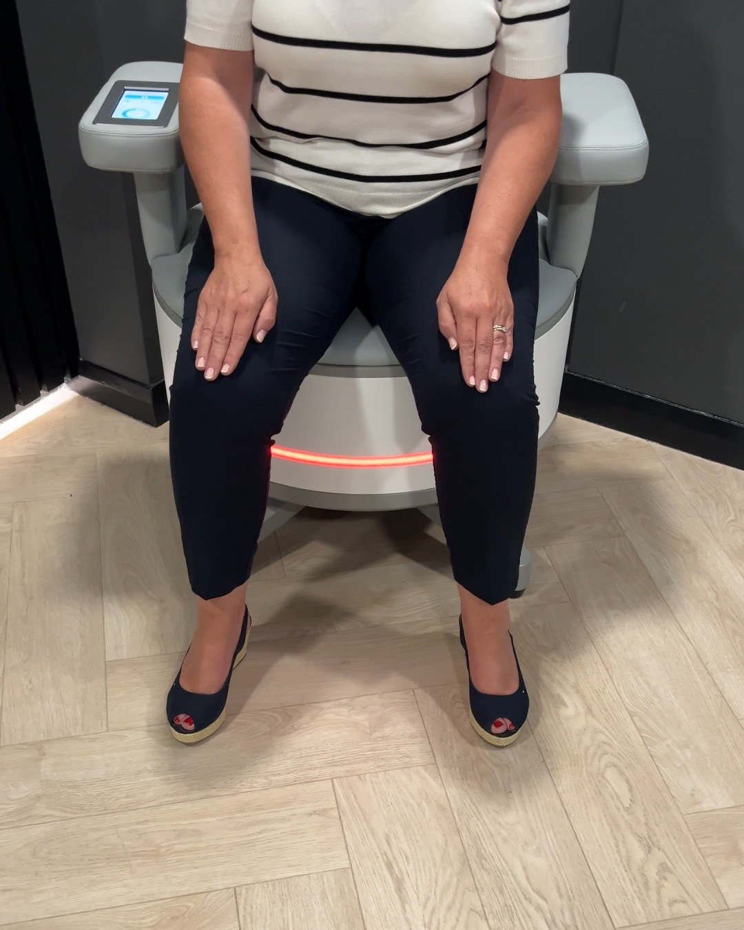 Front view of a fully clothed person on the Seat, with the armrest controls and illuminated base visible